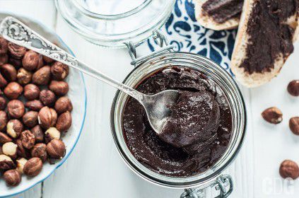 Nutella w słoiczku z łyżeczką, orzechy laskowe na talerzu, dwie kromki posmarowane