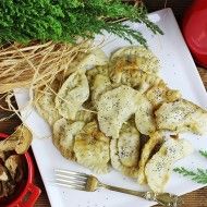 Pierogi z bryndzą n talerzy z widelcem i borowikami w osobnej miseczce