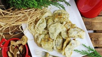 Pierogi z bryndzą n talerzy z widelcem i borowikami w osobnej miseczce