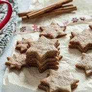 kruche ciasteczka ułożone na sobie, obok stoi czerwony kubek i kilka lasek cynamonu