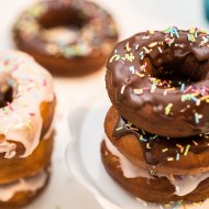 Donuty, pączki amerykańskie w lukrowej i czekoladowej polewie przyozdobione kolorowymi posypkami, ułożone jeden na drugim