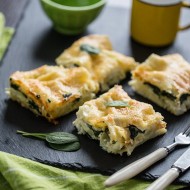 Lasagne z dorszem i szpinakiem na czarnym kamieniu. Podane ze sztućcami o białych trzonkach. i żółtym kubkiem