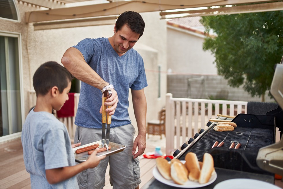 father and son grilling hot dogs together on backyard gas grill